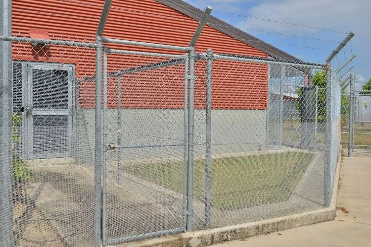 Galvanised chain wire gate with barbed topping at a brick building